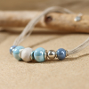 Zoom sur un collier en perles de céramique bleu, avec une perle en polymère bio et d'autres pièces en métal plaqué argent. 