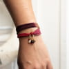 Le bracelet Nelly est un bijou tendance composé d'un ruban en soie teint à la main, de perles en nacre beige, de perles en verre violet et rouge et de perles en métal doré d'un flash d'or 24 carats.