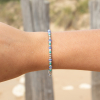 Le bracelet Marinière : un bracelet fin et lumineux composé de perles en verre blanches, de perles en verre émeraude, de perles en métal plaqué argent 999 et de perles rayées bleu marine et blanc.