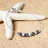 Forio est un bracelet composé d'un câble en métal plaqué argent 999 sur lequel est disposé des perles bleu gris. Une création Retour de plage.