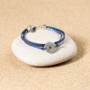 Le bracelet Vent est composé de 3 brins : un brin en polyester bleu marine, un cordon bleu marine et un ruban blanc et bleu marine. Il y a également une plaque rose des vents argentée.