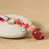 Porte-clefs composé d'une perle en verre rose, d'une perle orangé, d'une perle de rocaille rouge et d'un cordon en coton rouge.