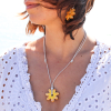 Jaune est un sautoir composé d'une perle en céramique jaune en forme de fleur, d'un cordon en lin beige et de perles en métal plaqué argent 999.