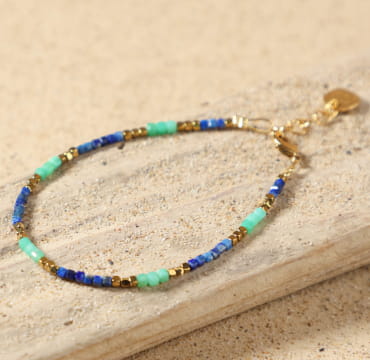 Bracelet Sormiou doré bleu dur posé à plat, montrant ses perles de lapis-lazuli bleu, d'amazonite verte et d'hématite dorée, avec fermoir mousqueton et médaille Retour de Plage, fait main en France.