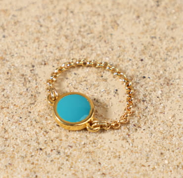 Bague Ouest dorée bleu turquoise posée à plat, montrant sa fine chaîne en métal doré à l'or fin 24 carats et son médaillon rond émaillé bleu vif, création artisanale française de Retour de Plage.