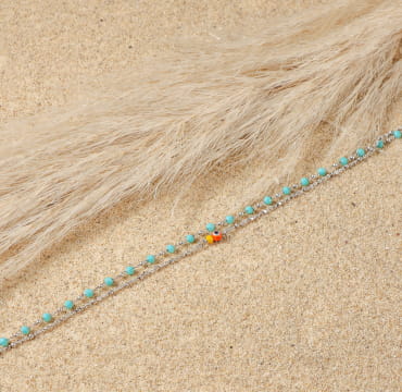 bracelet de cheville Bonita argenté avec perles bleues, posé sur sable doré