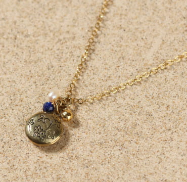 Collier Oma doré avec perle bleue sur fond sable – bijou fait main en France