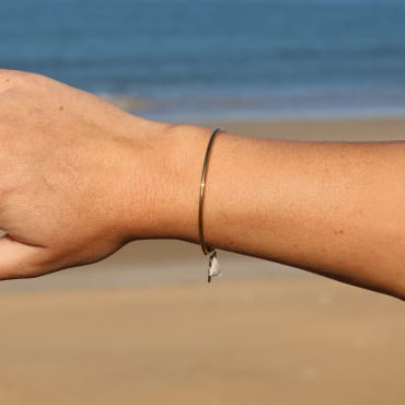 Bracelet jonc porté – bijou en métal doré avec perle émaillée, pompon beige en coton et perles en verre, fabrication artisanale française