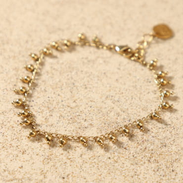 Bracelet Grelot doré posé à plat, montrant sa chaîne délicate ornée de petites perles rondes en métal doré 24 carats, avec médaille Retour de Plage, fait main en France.