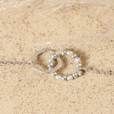 Détail du cercle en métal plaqué argent 999 enlacé dans un anneau de perles de rivière blanches et perles argentées du bracelet Isalie, sur fine chaîne argentée plaqué argent 999.