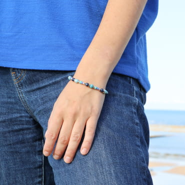 bracelet Konko doré avec perles kaki et fermoir en métal porté au poignet