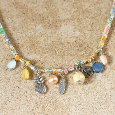 collier Annaé argenté avec perles jaunes et multicolores disposé en demi-cercle sur fond sable