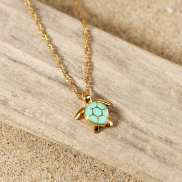 collier Bylot doré avec pendentif rond pierre turquoise posé sur fond sable