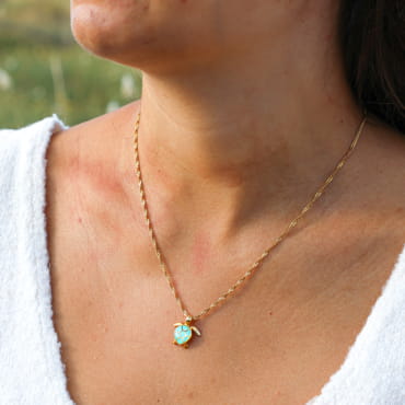 collier Bylot doré avec pendentif rond serti d’une pierre turquoise porté sur peau claire