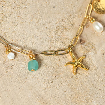 collier Dolcevita doré avec pendentifs vert d’eau sur sable clair