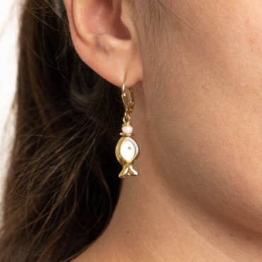 Une ode à l'Océan et à ses habitants... Craquez pour les boucles d'oreilles artisanales Wanda, composées de doux pendentifs dorés et blancs en forme de poisson. De délicates créations originales à porter en toute saison.