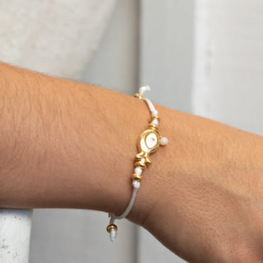 Un air de vacances à votre poignet avec le bracelet artisanal Wanda. Sa blancheur éclatante évoque les vagues scintillantes de l'océan. Orné d'un poisson doré, symbole de liberté, il incarne l'esprit marin.