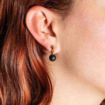 Atome est une paire de petites boucles d'oreilles composée d'un clou d'oreilles en métal doré d'un flash d'or 24 carats et d'un pendentif boule noir. Il s'agit d'une pièce unique fabriquée sur l'ïle d'Oléron.