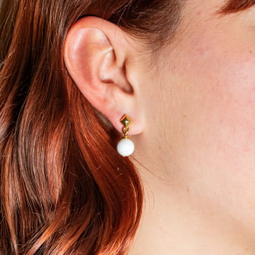 Atome est une paire de petites boucles d'oreilles composée d'un clou d'oreilles en métal doré d'un flash d'or 24 carats et d'un pendentif boule blanc. Il s'agit d'une pièce unique fabriquée sur l'ïle d'Oléron.