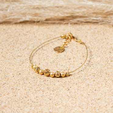 Bracelet Leslie posé sur le sable, reflet doré et élégance naturelle.