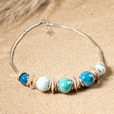 collier Coco en perles bleu ciel posé sur le sable, alternance de perles plates et rondes