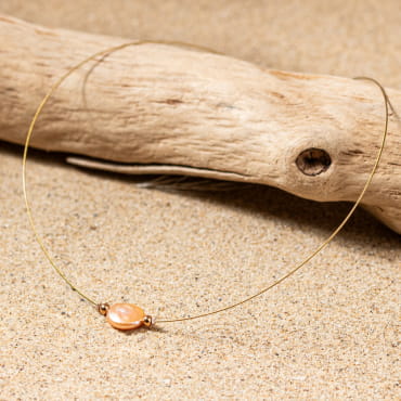 collier Flamand doré avec pendentif ovale rose saumon posé sur un bois flotté