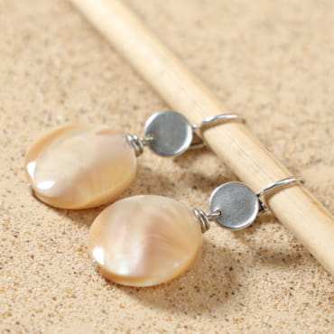 Boucles d’oreilles Calanque argentées posées à plat, montrant leur design élégant avec perle ronde en nacre beige, fait main en France – Retour de Plage