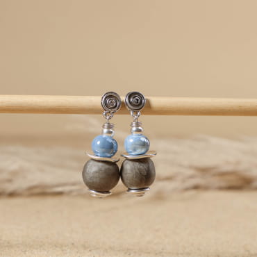 boucles d’oreilles Douhet argenté ornées de perles bleu Montana posées sur tissu clair