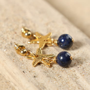 Boucles d’oreilles Niki dorées posées à plat, montrant leur design élégant avec étoile de mer et perle de dumortiérite bleu marine, fait main en France – Retour de Plage
