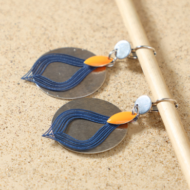 Boucles d’oreilles Sibylle argentées posées à plat, montrant leur design élégant avec perle calisson émaillée orange, pendentif rond en métal plaqué argent 999 et pendentif goutte bleu, fait main en France – Retour de Plage