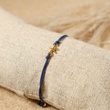 bracelet Transat doré avec cordon bleu marine posé sur tissu clair