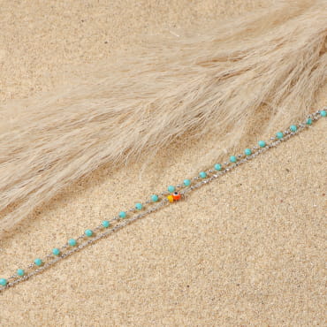 bracelet de cheville Bonita argenté avec perles bleues, posé sur sable doré