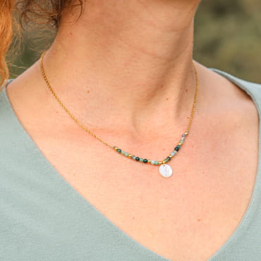 Collier doré orné de perles vertes et multicolores, porté sur un cou délicatement bronzé.