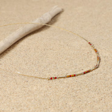Collier rouge et doré allongé sur le sable, bijou fabriqué à la main en France