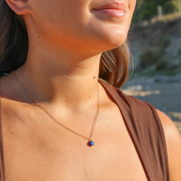 collier Soft doré avec perles bleues porté sur décolleté avec haut marron