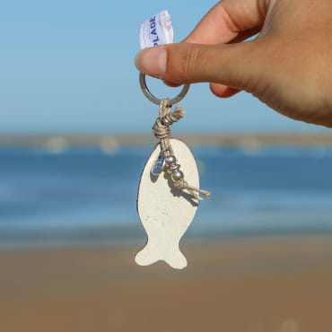 porte-clés Sardinhas argenté avec poisson blanc tenu en main sur fond marin