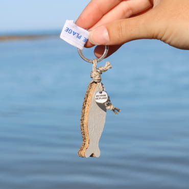 porte-clés Sardinhas argenté et blanc tenu en main sur fond de ciel clair