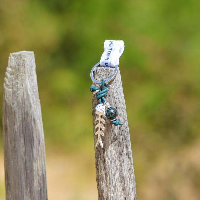 Porte-clés artisanal en métal argenté avec cordon bleu pétrole, orné de perles marines. Fabrication française.
