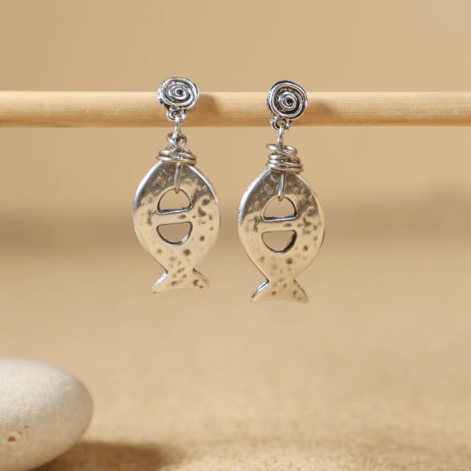 Paire de boucles d’oreilles argentées en forme de poisson, posées sur le sable – fabrication française