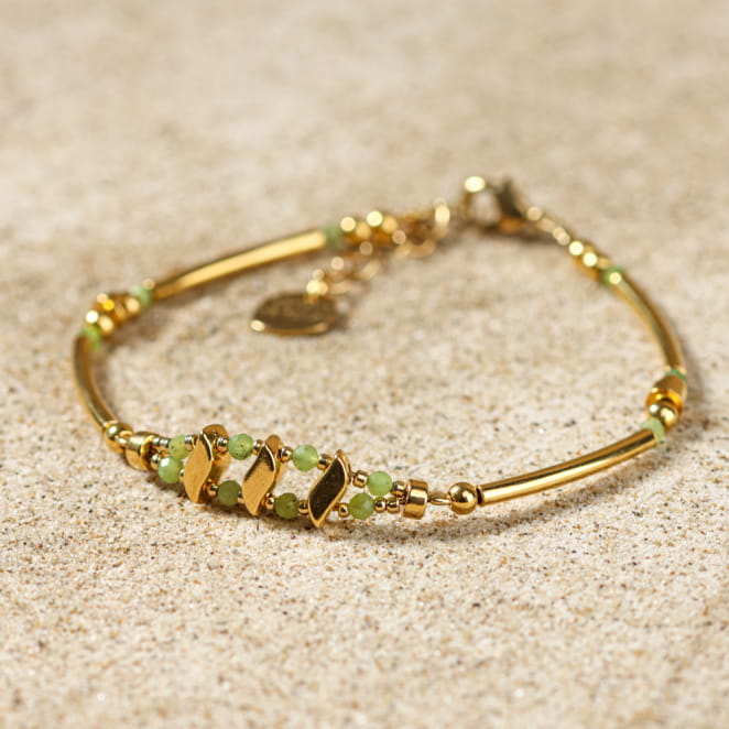 Bracelet doré et vert Anisha posé sur le sable – création faite main en France
