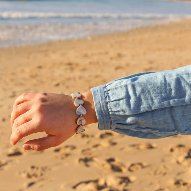 Bracelet Love argenté et perles grises porté au poignet sur fond de sable – bijou fait main