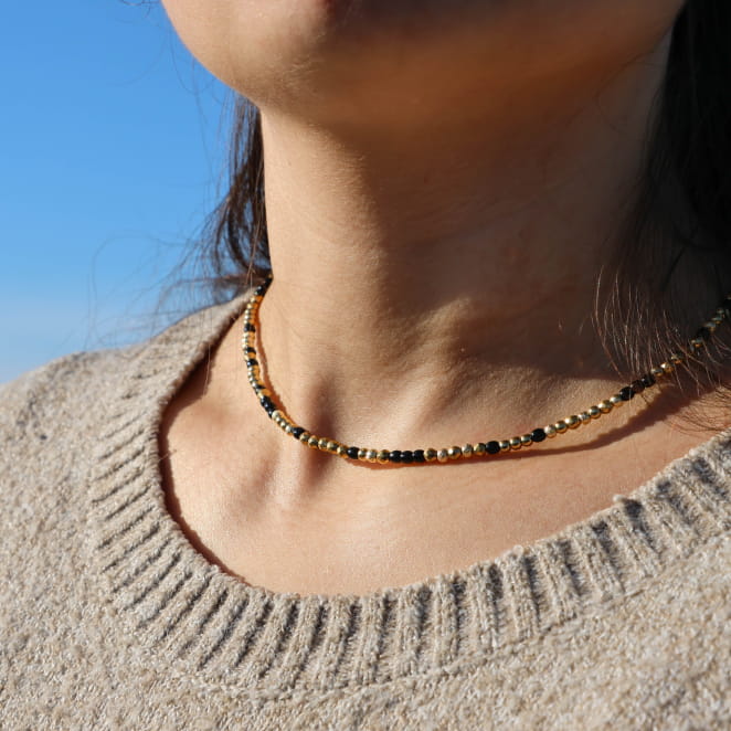 Collier Luciole doré et perle noire porté sur haut côtelé – fabrication artisanale française