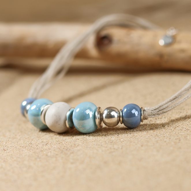 Zoom sur un collier en perles de céramique bleu, avec une perle en polymère bio et d'autres pièces en métal plaqué argent.