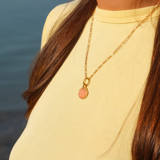 collier Caliopee doré orné d’un pendentif corail porté sur haut beige