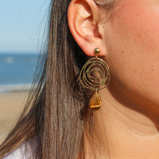 Boucles d'oreilles Isabella portées – bijou en métal doré avec spirale ajourée et perle goutte en œil de tigre, fabrication artisanale française