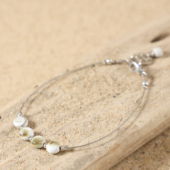 Bracelet Ajaccio argenté blanc posé à plat, montrant son design élégant avec perles en forme d'œil de Sainte-Lucie et petites perles en métal plaqué argent 999, sur câble en acier argenté, médaille Retour de Plage.