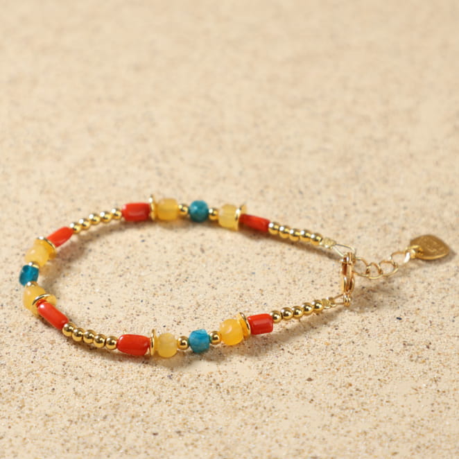 Bracelet Bologne doré multicolore posé à plat, montrant ses perles de jade jaune, d'apatite bleue, de corail rouge et ses rondelles en métal doré à l'or fin 24 carats, avec médaille Retour de Plage.