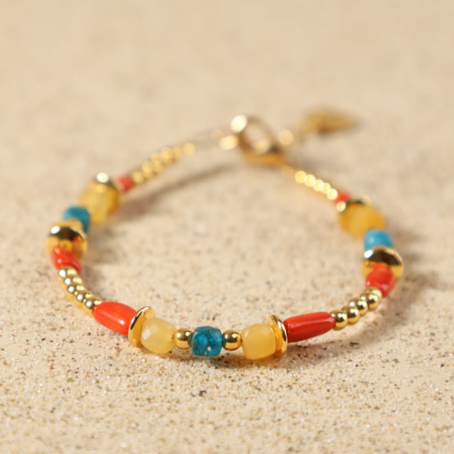 Gros plan sur les perles de jade jaune, d'apatite bleue, de corail rouge et les rondelles en métal doré à l'or fin 24 carats du bracelet Bologne, avec médaille Retour de Plage