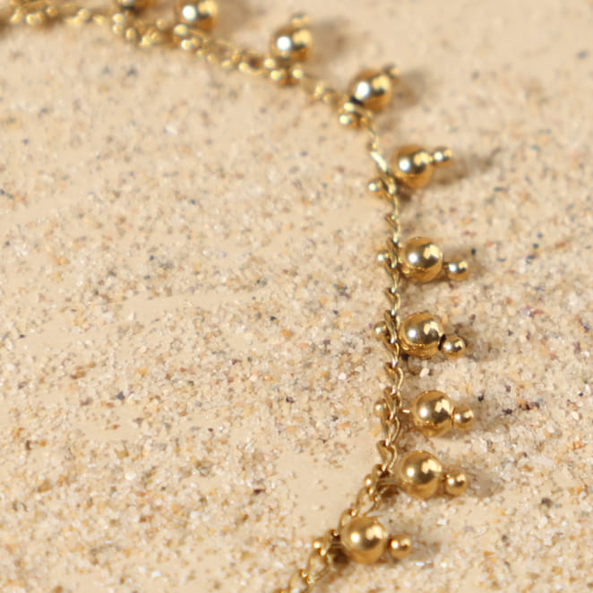 Gros plan sur les petites perles rondes en métal doré 24 carats du bracelet Grelot, avec médaille Retour de Plage, fabrication artisanale sur l'île d'Oléron.