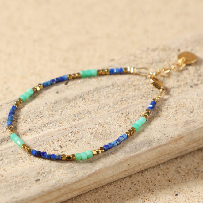 Bracelet Sormiou doré bleu dur posé à plat, montrant ses perles de lapis-lazuli bleu, d'amazonite verte et d'hématite dorée, avec fermoir mousqueton et médaille Retour de Plage, fait main en France.